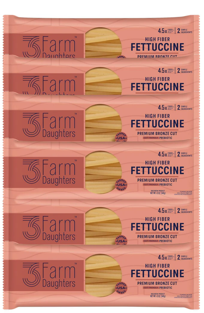 Multiple packages of 3 Farm Daughters Fettuccine pasta on a pink background