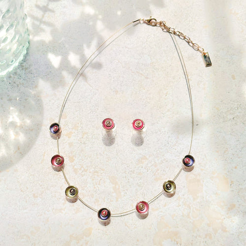 Adjustable Choker Necklace against a textured stone background with a brown steel cable chain and seven rose gold plated circular flower charms painted in purple, pink, and gray with a pair of matching circular flower earrings in pink and gray