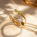 18K vermeil gold birthstone initial rings with faceted gemstones and leaf charms, shown with soft natural shadows.