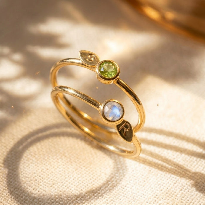 18K vermeil gold birthstone initial rings with faceted gemstones and leaf charms, shown with soft natural shadows.