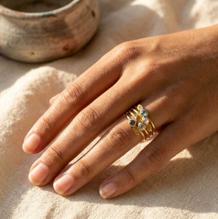 Custom birthstone stacking rings worn on hand with colorful gemstones and leaf initial charms, a meaningful personalized ring gift.