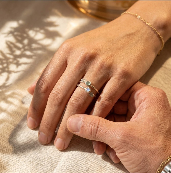 Personalized birthstone leaf stacking ring worn on hand, custom with a 3mm gemstone and stamped initial charm representing his and her birthstones and nitials