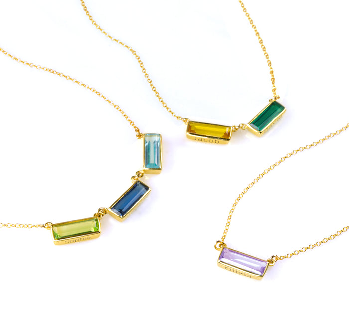 Personalized baguette-cut birthstone bar necklaces in sterling silver, gold filled, and rose gold, each with rectangular bezel settings. Customize with engraved names or secret messages to create a sentimental birthstone jewelry gift for mom or grandmother. Choose from January Garnet, February Amethyst, March Aquamarine, May Emerald, July Ruby, September Sapphire, December Blue Topaz, and more to represent your family.