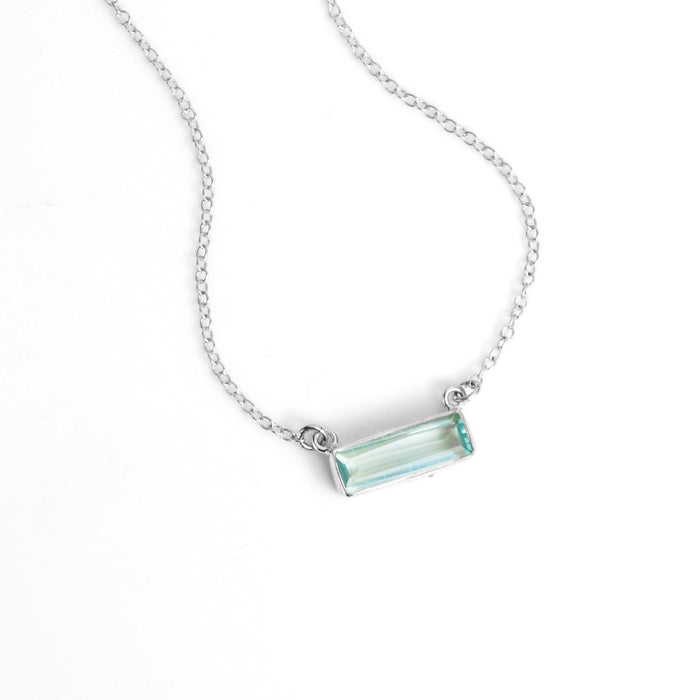 Single sterling silver cable chain with horizontal blue topaz december birthstone adira bar necklace on white background