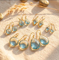 Faceted blue topaz earrings in seven teardrop, round, and geometric styles on cream fabric.