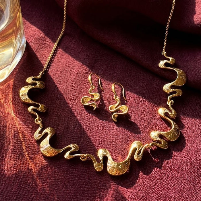 Boho wave necklace and earrings set in gold on burgundy fabric with organic wavy statement design