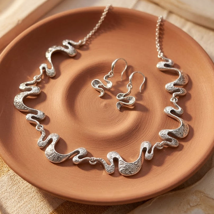 Silver boho wave necklace and matching earrings displayed on a terracotta dish