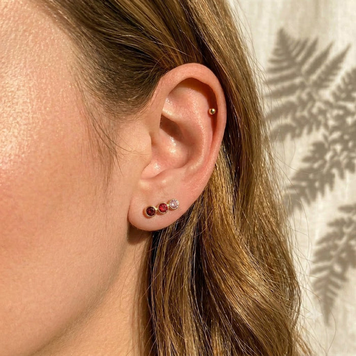 Tiny custom birthstone stud earrings worn in a second ear piercing, showing a minimalist everyday style for personalized gemstone earrings in gold or sterling silver.