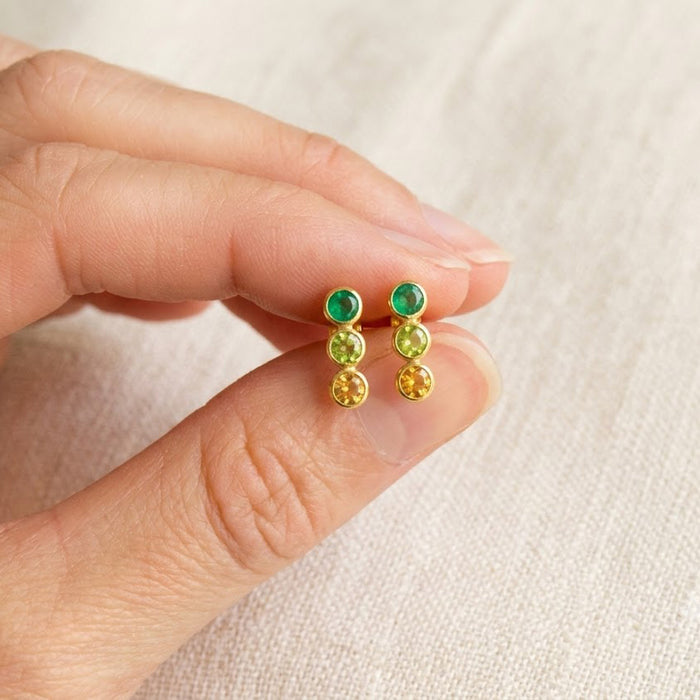 Hand holding custom three-stone birthstone bar stud earrings with green gemstone choices, a meaningful personalized earring design for moms, sisters, or friends.