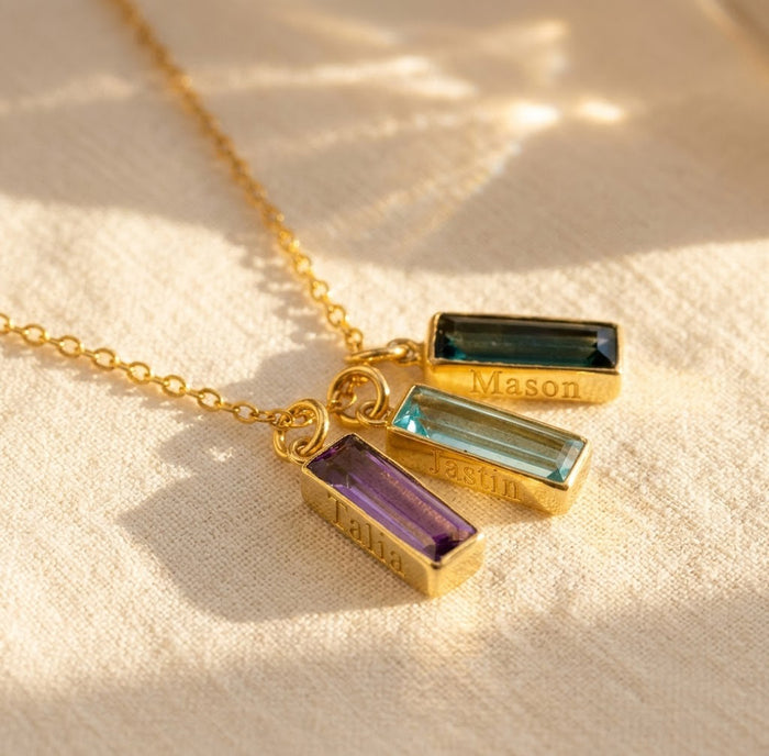Custom birthstone name bar necklace with engraved names and colorful gemstone charms on a gold chain.