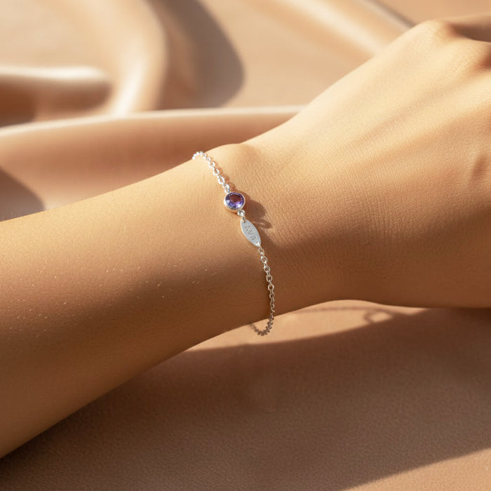 Model wearing dainty birthstone name bracelet with one gemstone and engraved charm.