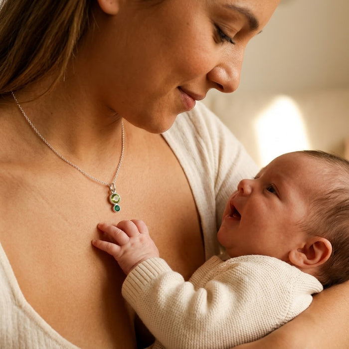 Mother wearing a personalized birthstone necklace while holding her baby, showing a meaningful new mom necklace with children’s birthstones on a dainty gold chain.