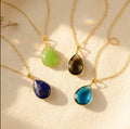Custom birthstone necklace with teardrop pendant in multiple gemstone colors on cream background