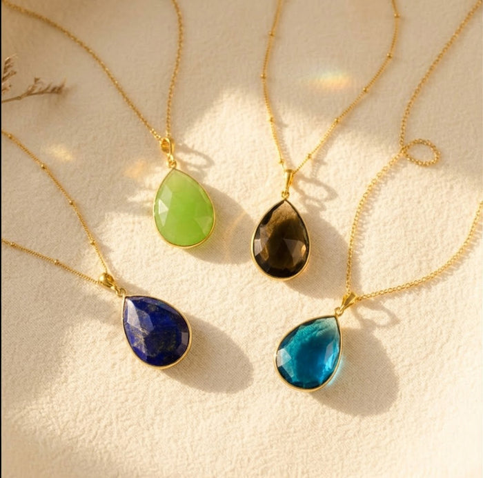 Custom birthstone necklace with teardrop pendant in multiple gemstone colors on cream background
