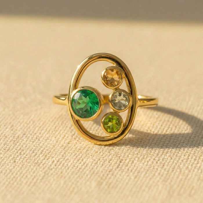 Custom birthstone ring for Mom with one larger green mom stone and three smaller kids birthstones in a gold oval setting.