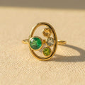 Custom birthstone ring for Mom with one larger green mom stone and three smaller kids birthstones in a gold oval setting.