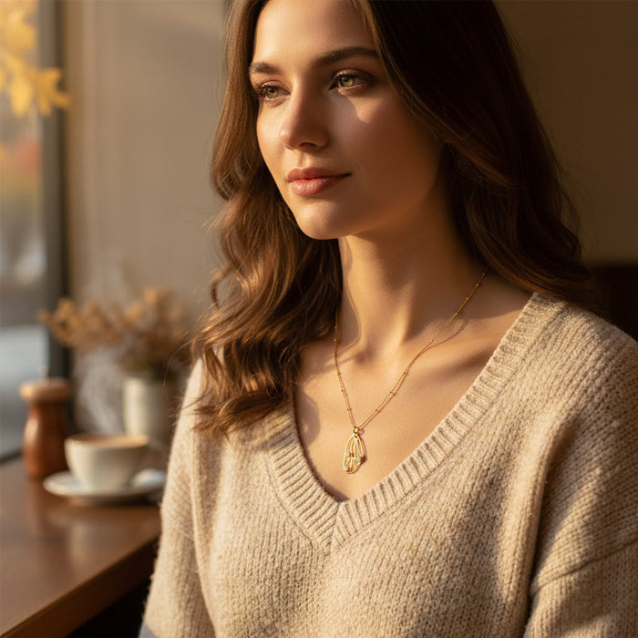 Cozy lifestyle shot of woman in sweater wearing butterfly wing birthstone necklace, personalized dainty jewelry gift idea for sister, friend, or girlfriend