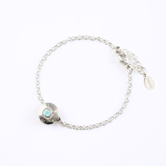 A 925 sterling silver donut bracelet with an aqua chalcedony stone and the letter "M" engraved on the bottom of the disc rests against a white background. This bracelet is hypoallergenic and is sure to make the day of anyone who receives this as a gift! This is the perfect thing for Mother's Day!