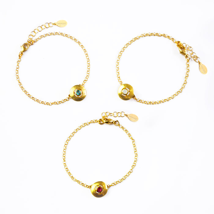 Three gold engraved disc bracelets with blue topaz, moonstone and ruby quartz rest against a white background. December birthstone jewelry, June birthstone jewelry, July birthstone jewelry.
