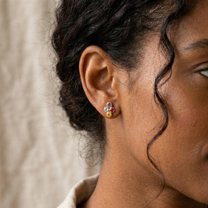 Woman wearing tiny four birthstone stud earrings personalized with colorful natural gemstones in a delicate cluster