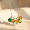 Custom mom birthstone necklace with green, blue, and peridot teardrop charms and gold initial discs on a warm neutral background.