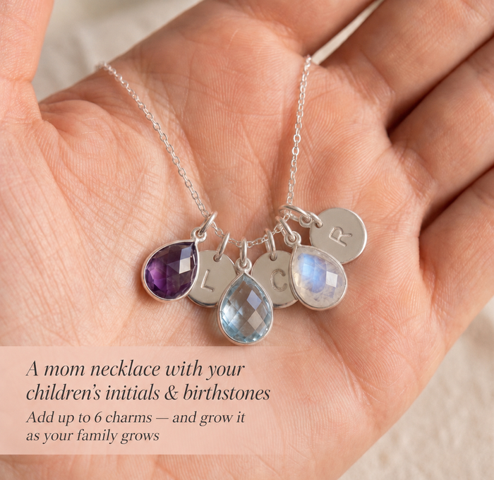 Close-up of a silver custom mom necklace with teardrop birthstones and initial charms in the palm of a hand.