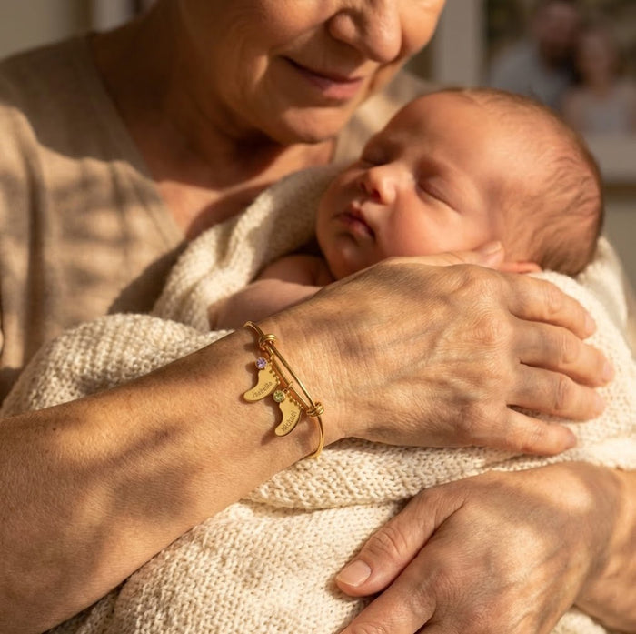 grandma holding a newborn while wearing a personalized footprint bangle bracelet with birthstone and name charms.