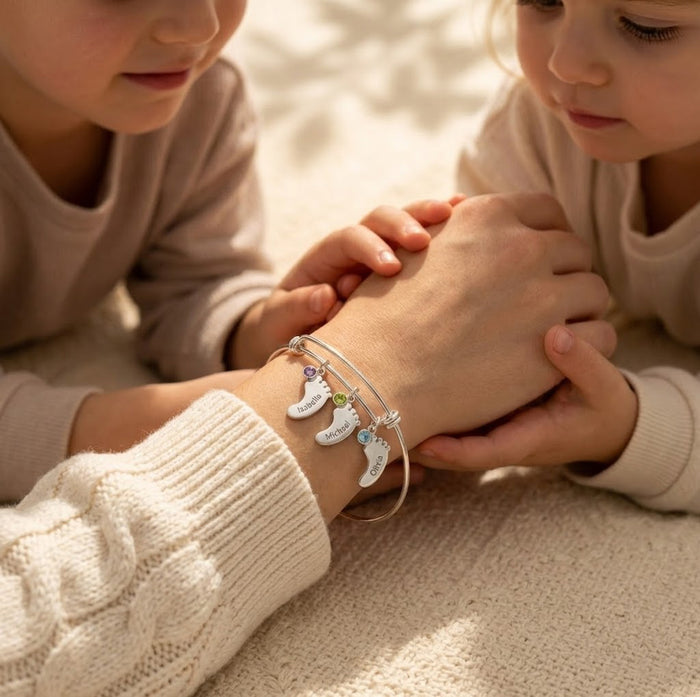 Mother and child holding hands while wearing a personalized footprint bracelet with engraved name charms and birthstones.