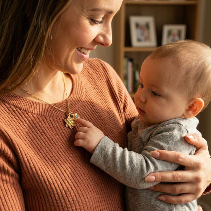 Mother wearing personalized birthstone flower necklace while holding baby, custom mom jewelry with kids birthstone flower charms.