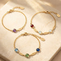 Dainty personalized birthstone bracelet with one name charm displayed on soft neutral fabric.
