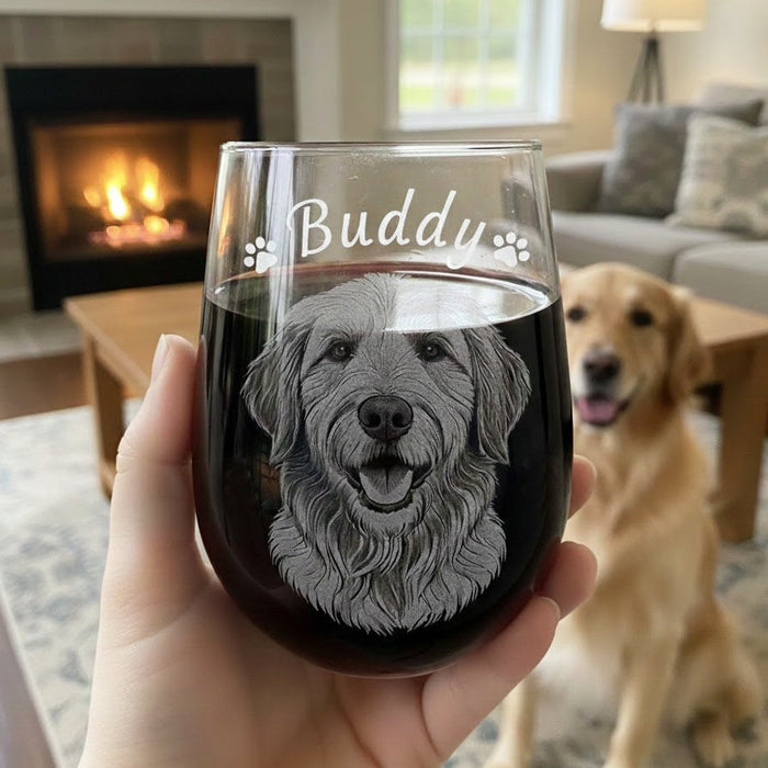 Custom pet portrait wine glass engraved with dog illustration, name “Buddy” and paw prints, filled with red wine in a cozy living room; personalized stemless wine glass gift for dog mom, dog dad, pet memorial or animal lover.