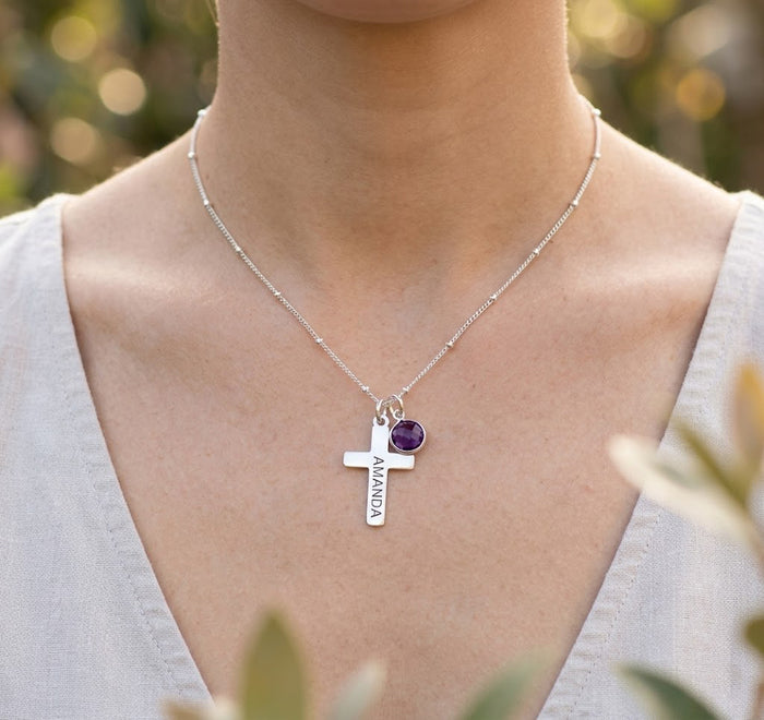Close-up of woman wearing engraved cross and birthstone necklace, delicate personalized religious necklace