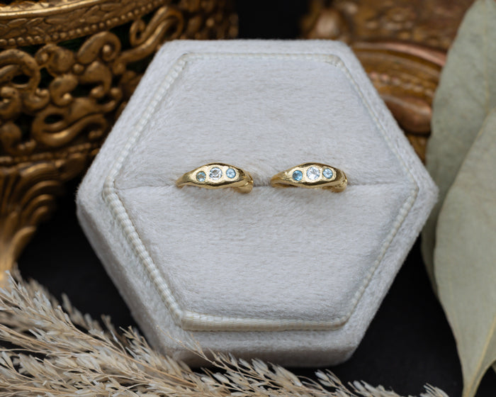 Gold hoop earrings with blue topaz accents on a white hexagonal stand with decorative elements.