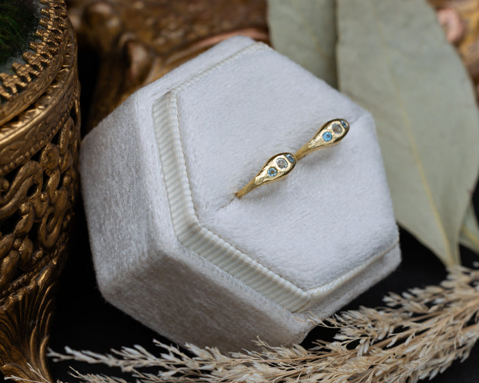 Gold hoop earrings with blue topaz accents on a white hexagonal stand with decorative elements.