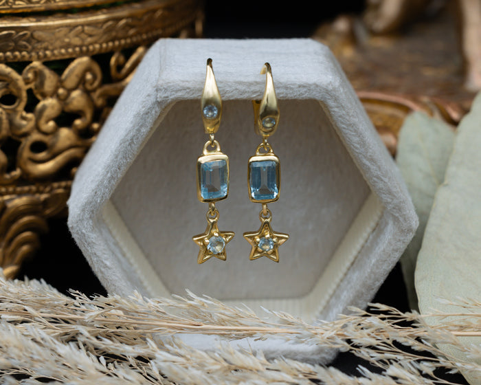 Gold earrings with star and blue topaz gemstone accents on a decorative stand.