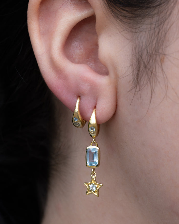 Gold earrings with blue topaz accents worn by a person