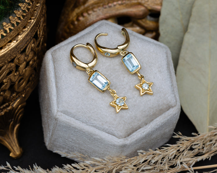 Gold earrings with star and blue topaz gemstone accents on a decorative cushion