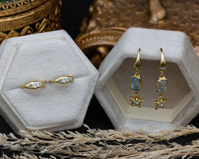 Gold earrings set of earrings on a hexagonal cushion against a dark background.