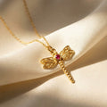 Gold dragonfly birthstone necklace closeup on soft beige fabric, dainty insect pendant with marquise wing stones and a center birthstone, personalized custom birth month jewelry in 925 sterling silver or gold vermeil, minimal everyday necklace gift for her, nature lover, birthday, anniversary, memorial keepsake