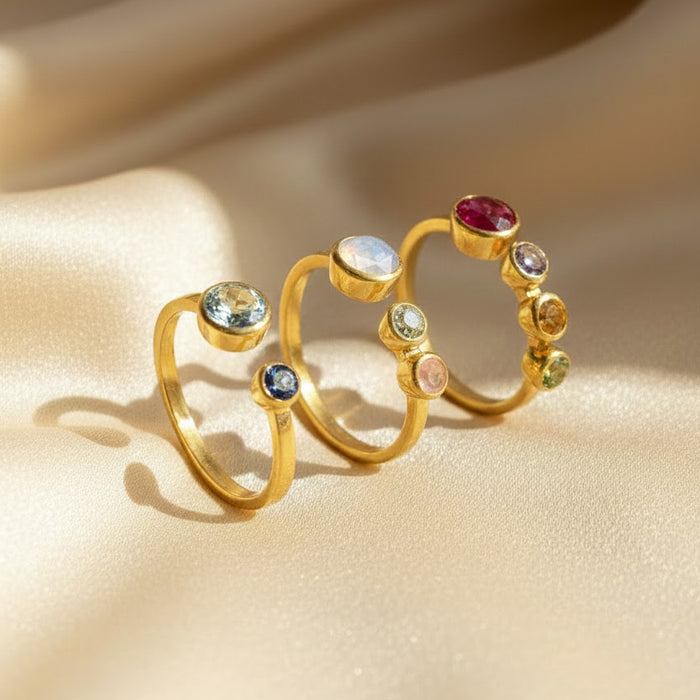 Close-up of adjustable two birthstone ring on soft ivory fabric, personalized open ring with bezel set gemstones in yellow gold