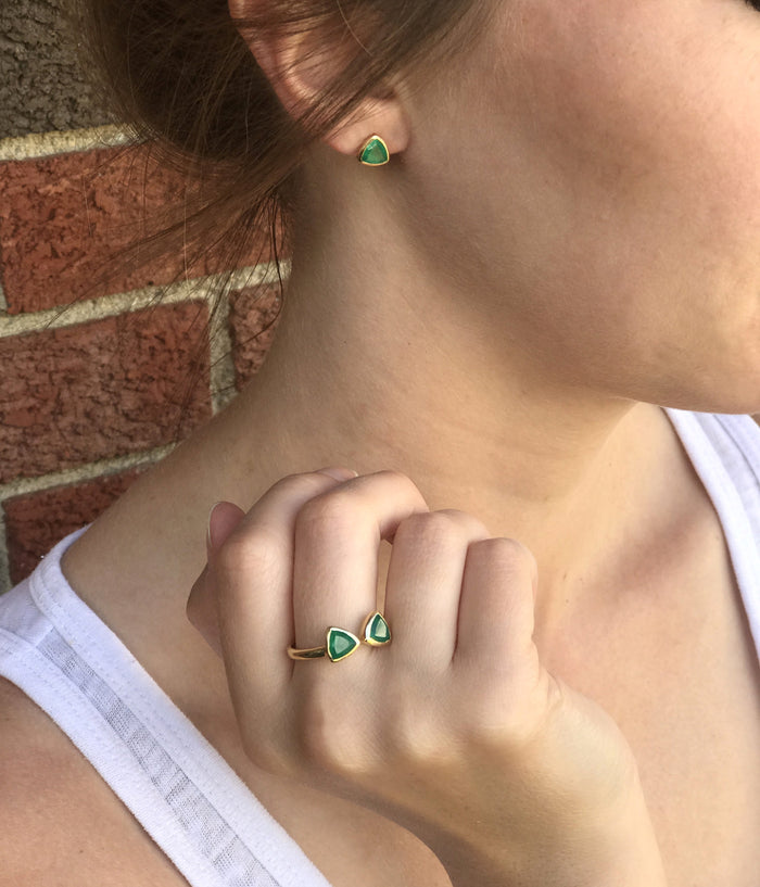 A person wears a set of green onyx triangle stud earrings and a matching green onyx triangle bow tie ring.  Customizable birthstone ring, adjustable triangle bow tie ring, personalized gemstone jewelry, sterling silver triangle ring, gold bow tie ring, rose gold triangle ring, mix-and-match birthstones, unique double triangle ring, adjustable gemstone ring, custom bow tie jewelry, bespoke birthstone ring, chic triangle-cut ring, elegant birthstone ring, unique gemstone gift, customizable stacking ring