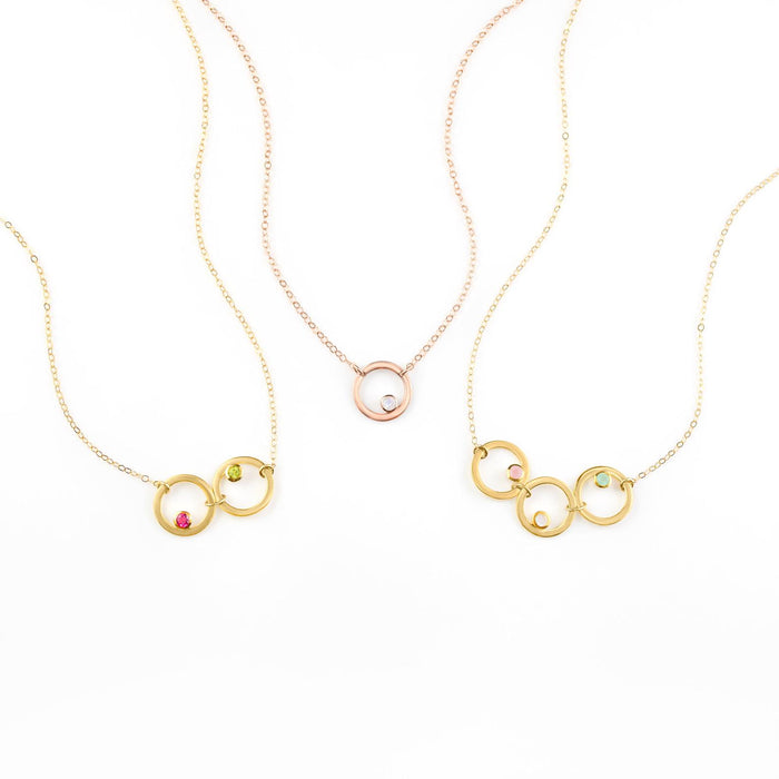 Collection of open circle eden necklaces from left to right. One gold filled necklace with ruby and peridot birthstones, one rose gold necklace with moonstone, and one gold necklace with pink chalcedony, moonstone and aqua chalcedony birthstones.