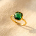 Emerald quartz cushion ring in gold shown on warm beige fabric with a deep green 9mm gemstone and slim minimalist band.