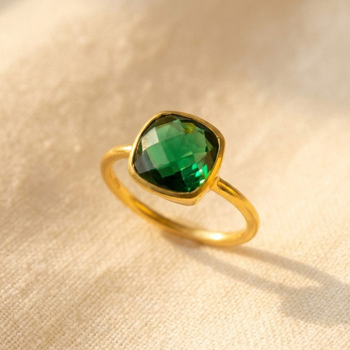 Emerald quartz cushion ring in gold shown on warm beige fabric with a deep green 9mm gemstone and slim minimalist band.