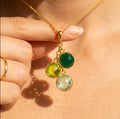 Family birthstone cluster necklace with green gemstones in yellow gold worn on model