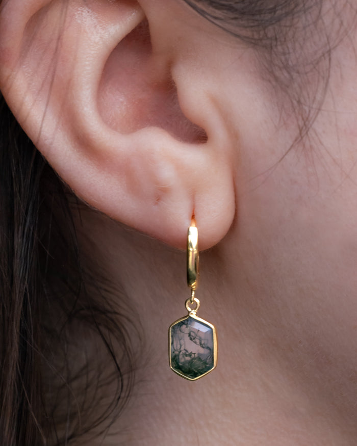 Gold earring with a green gemstone worn by a person