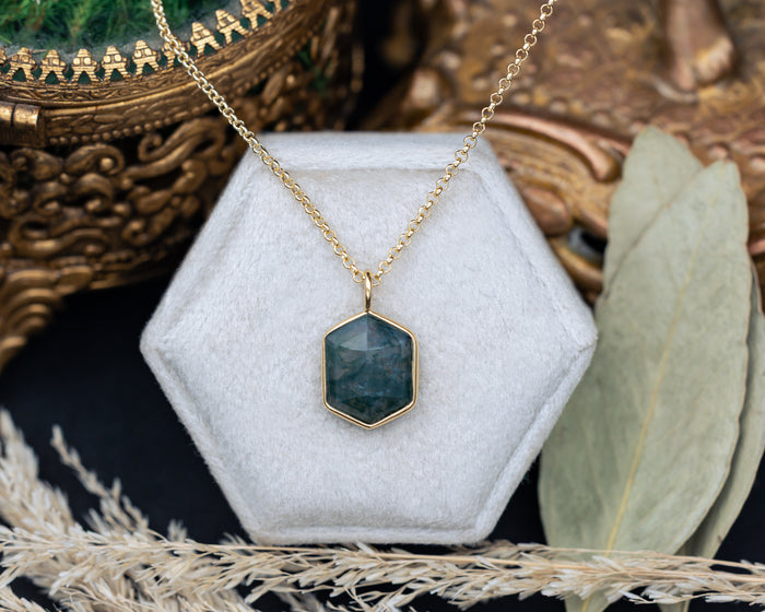 Necklace with a hexagonal moss agate pendant on a white hexagonal stand with a decorative background