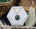 Necklace with a hexagonal moss agate pendant on a white hexagonal stand with a decorative background