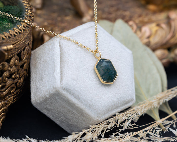 Necklace with a hexagonal pendant on a white hexagonal stand with a decorative background