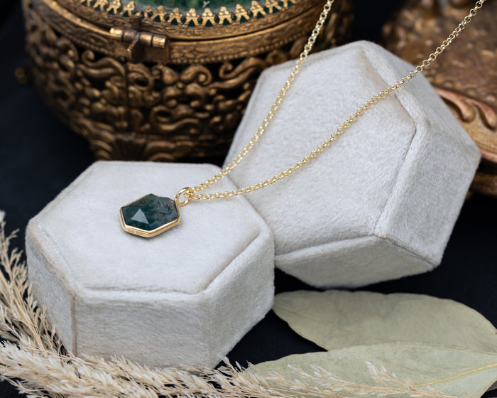 Necklace with a hexagonal pendant on a white hexagonal stand with a decorative background